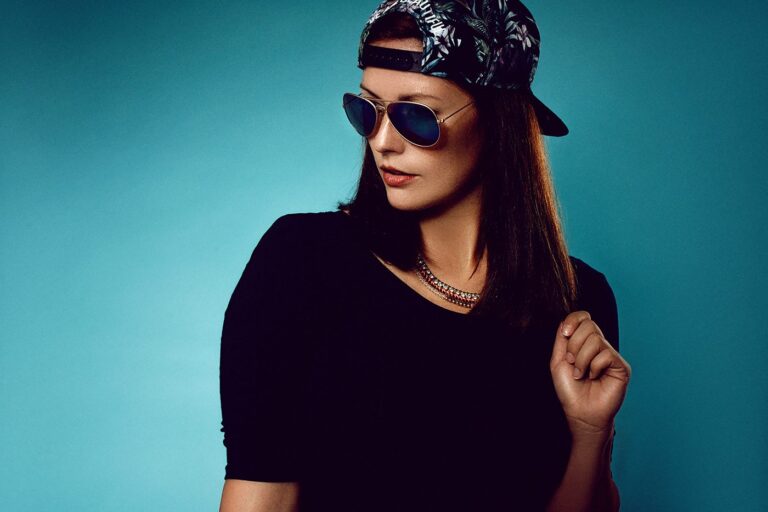 Model mit Cap und Sonnenbrille vor türkisem Hintergrund